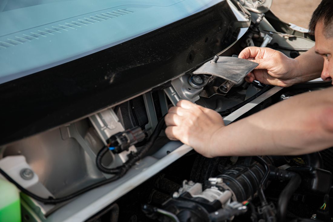 Hands inspecting components beneath a vehicle hood
